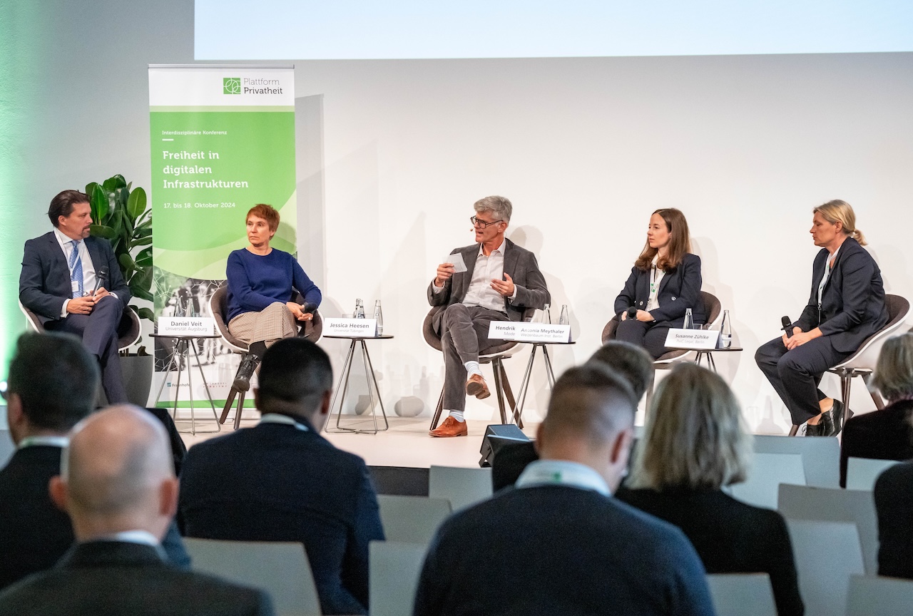 Eine Podiumsdiskussion mit fünf Personen auf einer Konferenzbühne.