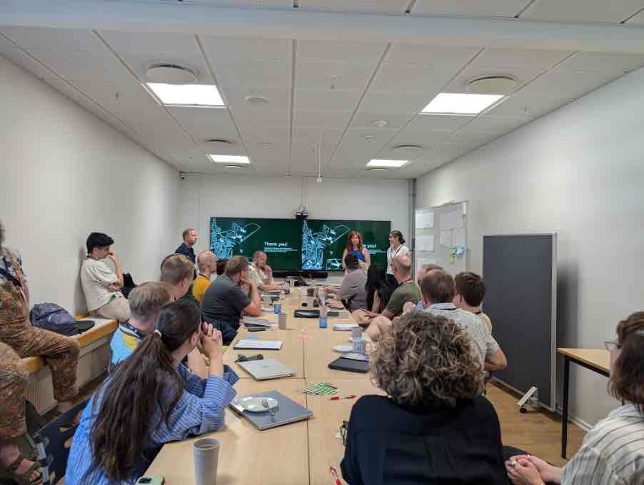 Blick durch den Konferenzraum der DASTS-Jahrestagung in Kopenhagen: Teilnehmende sitzen an einem langen Tisch, zwei Vortragende stehen vor Bildschirmen mit der Aufschrift „Thank you!“.